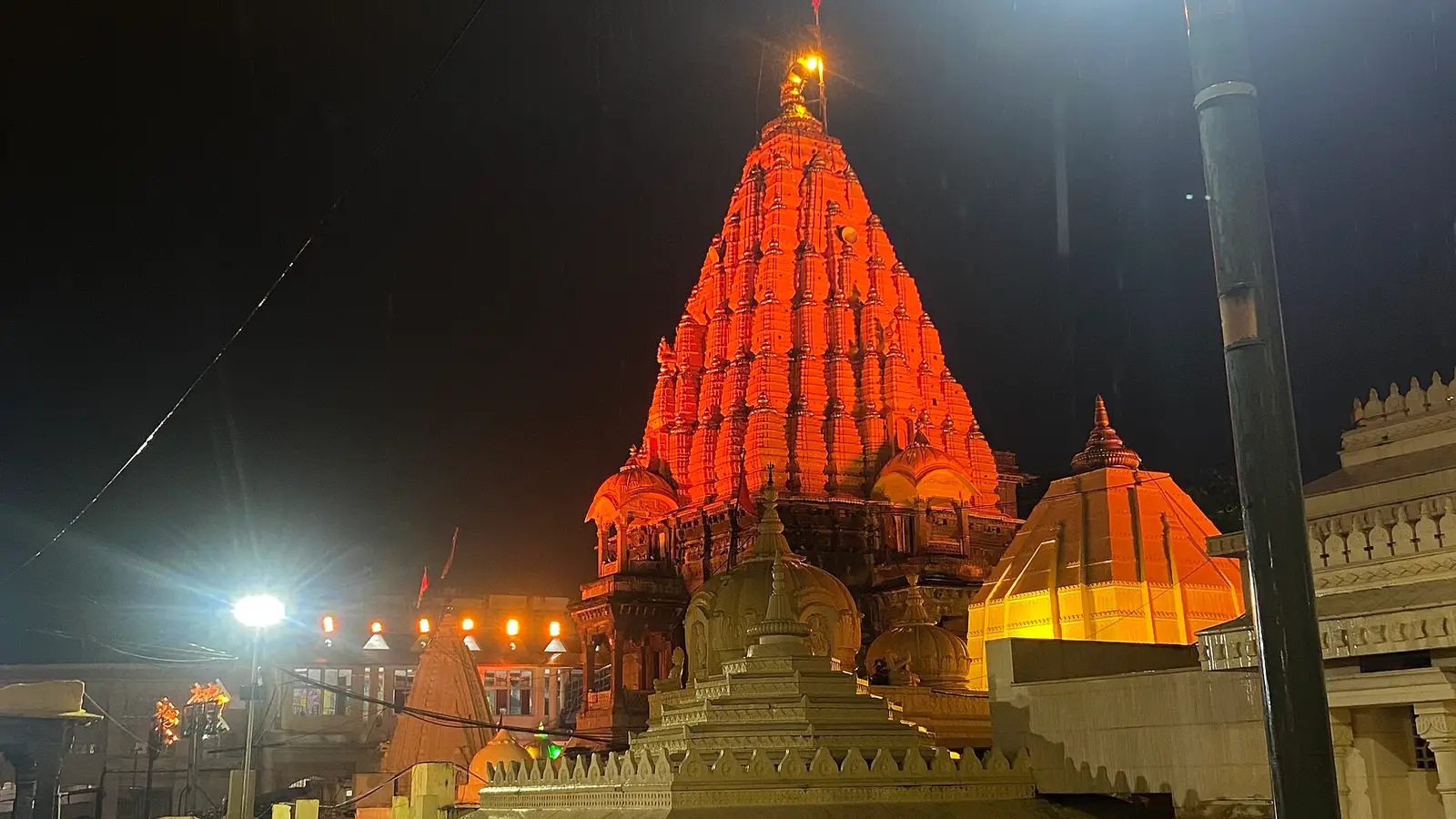 The Mahakaleshwar temple shikhara in Ujjain lit orange before dawn, with steel queue railings and a street lamp in the foreground
