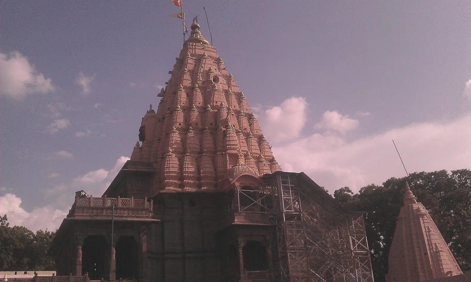 The tall carved sandstone shikhara of Mahakaleshwar temple in Ujjain against a pink-tinted sky with clouds