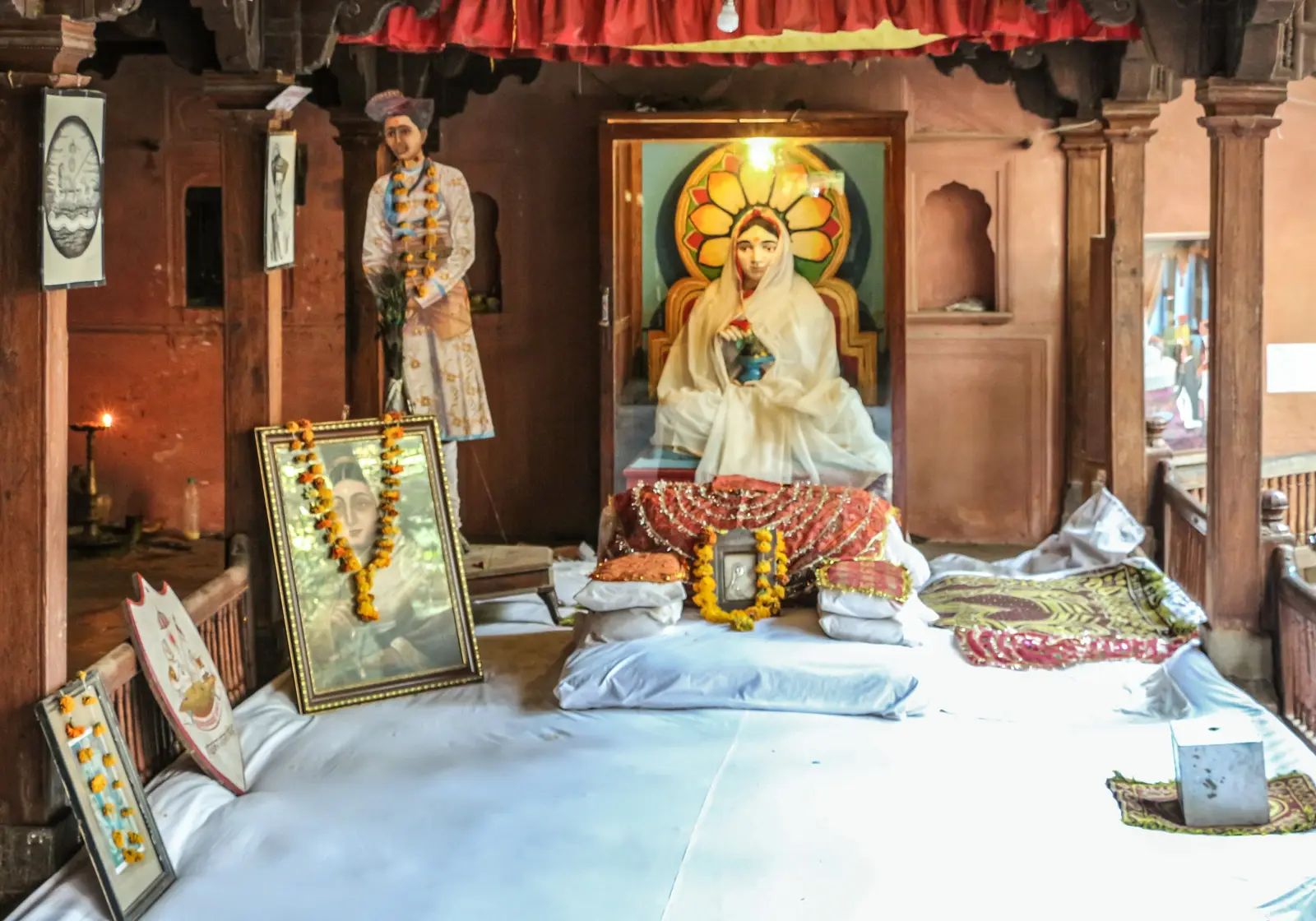Life-size statue of Ahilyabai Holkar in a white sari seated on the gaddi in the Rajwada at Maheshwar, with garlands and framed portraits around her
