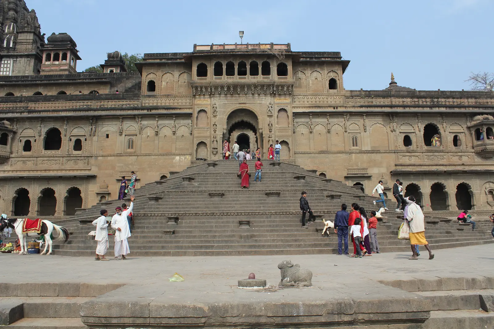 The wide stone stairway rising from Ahilya Ghat to the fort gate at Maheshwar, with visitors on the steps and the Ahilyeshwar temple shikhara at top left