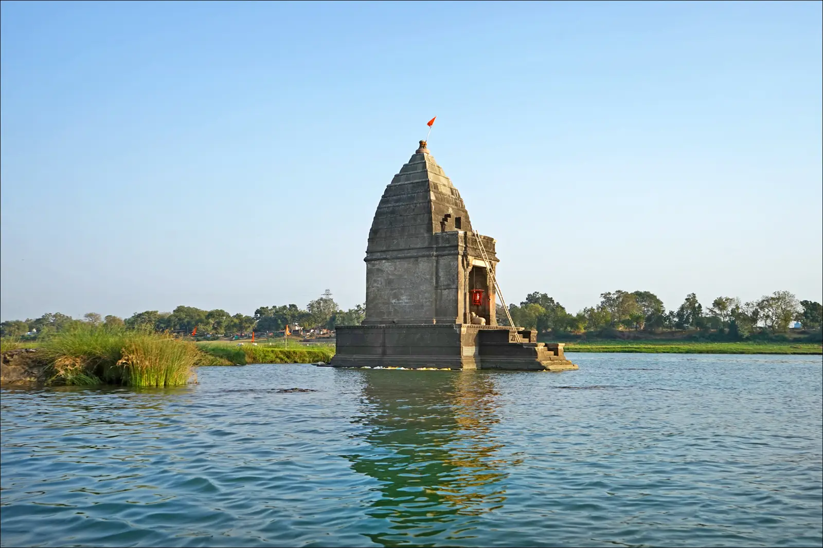 The small stone Baneshwar temple standing on a rock in the middle of the Narmada at Maheshwar, with a small flag on its spire