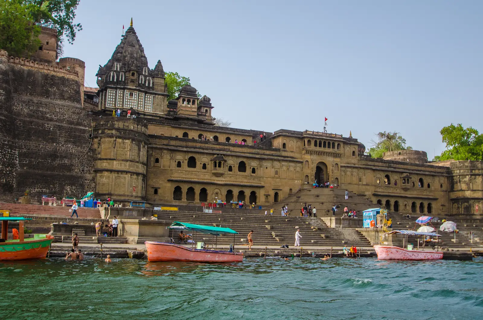 Ahilya Fort's walls and palace front with the Ahilyeshwar temple shikhara above, rising over the Narmada ghats at Maheshwar, with boats in the foreground