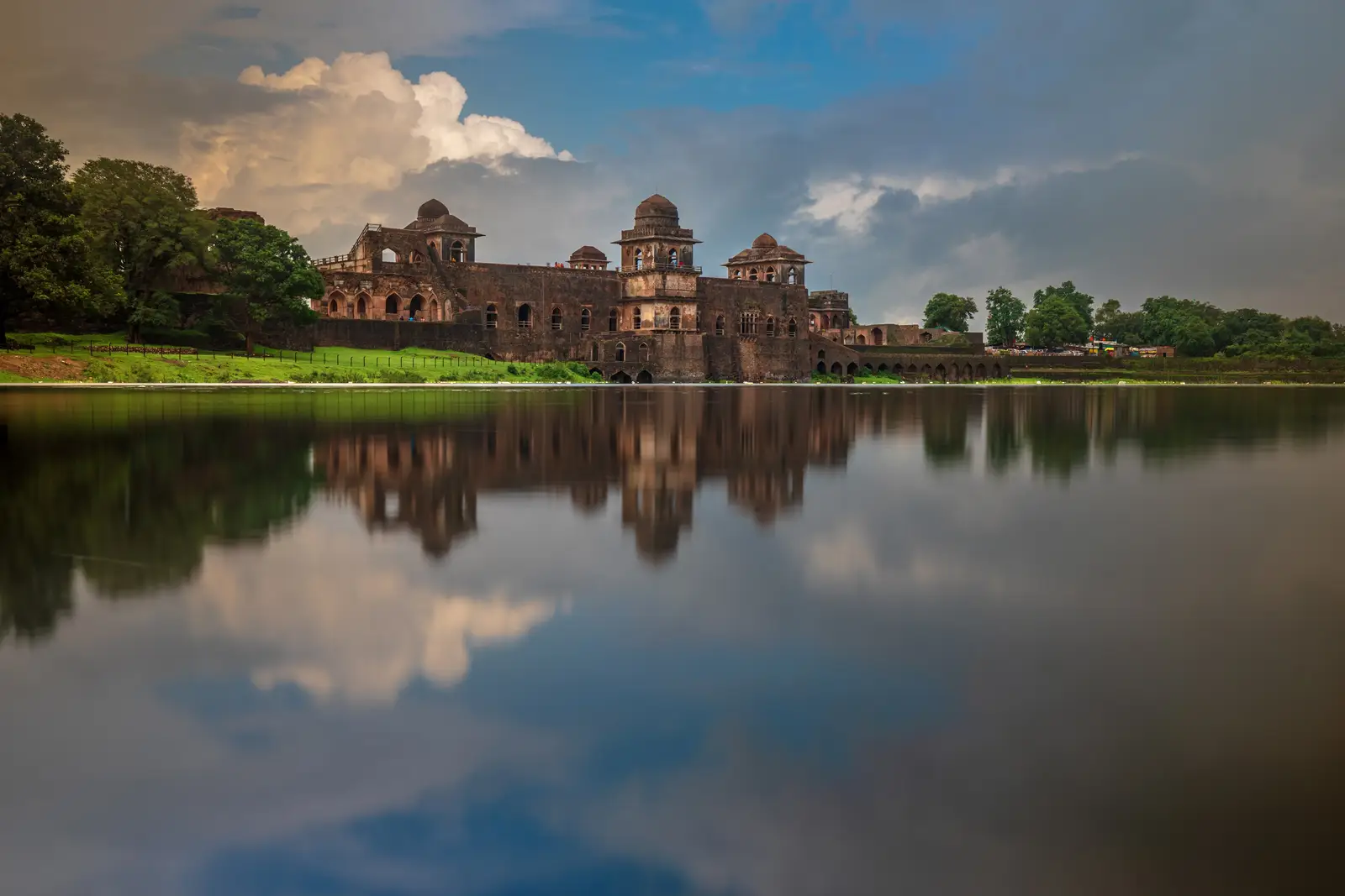 Jahaz Mahal in Mandu reflected in the full lake beside it after the monsoon rains, under a cloudy sky
