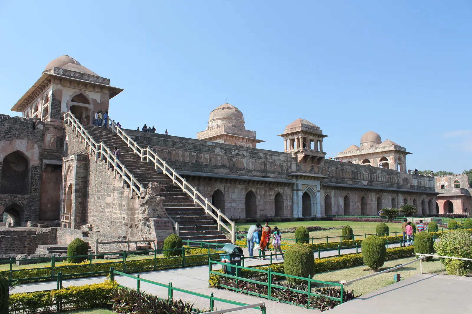 External stone stairway climbing to the rooftop pavilions of Jahaz Mahal, with lawns and visitors in the Royal Enclave, Mandu