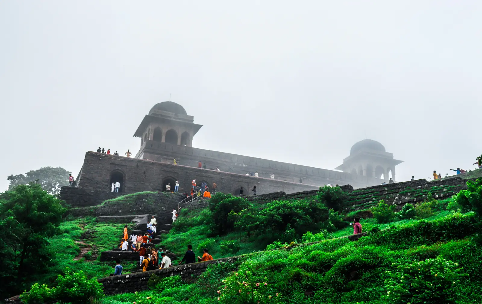 Rani Roopmati's Pavilion in Mandu wrapped in monsoon mist above a green hillside, with visitors climbing the slope