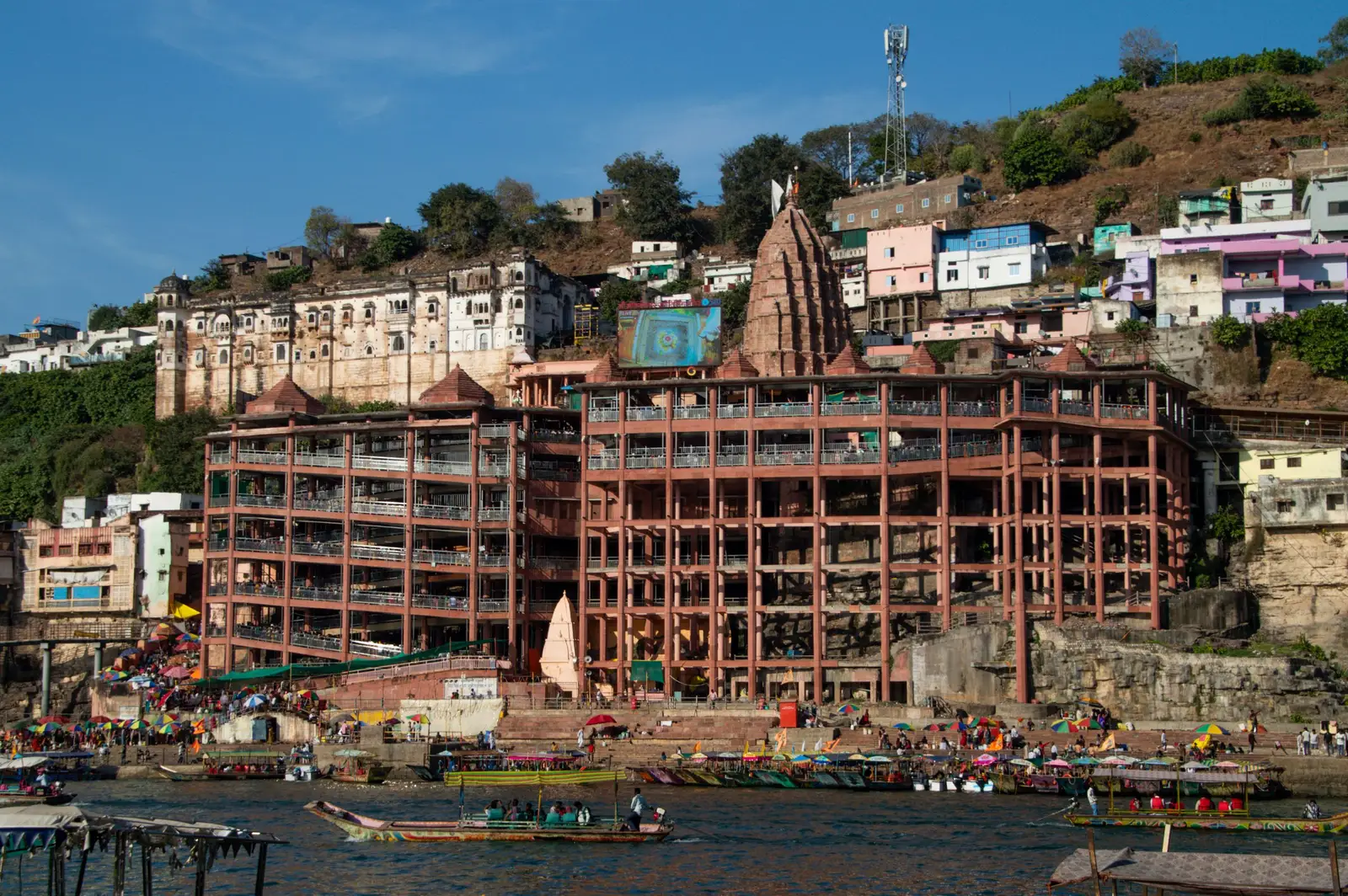 Omkareshwar temple complex and its shikhara rising above the Narmada ghats, with boats moored at the water's edge