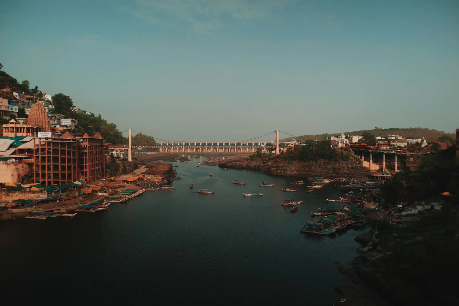 Aerial view of the Narmada at Omkareshwar with the Jhula Pul suspension bridge, boats on the river and the temple complex on the left