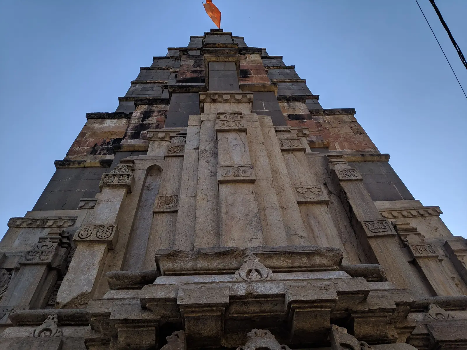 Carved stone shikhara of the Mamleshwar temple at Omkareshwar against a clear blue sky, with a saffron flag on top