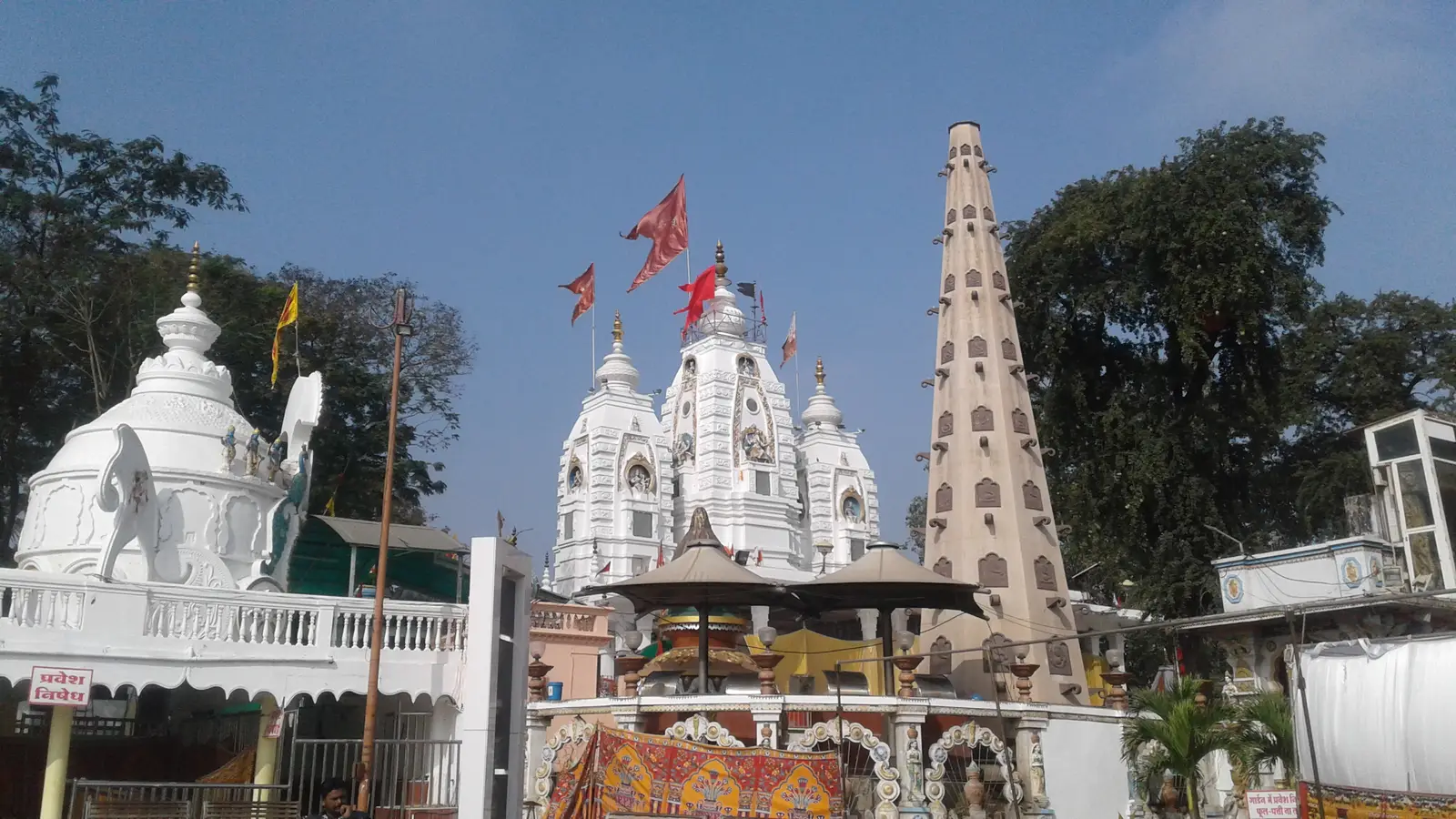 White shikharas of the Khajrana Ganesh Temple in Indore with saffron flags and a tall carved stone tower against a blue sky