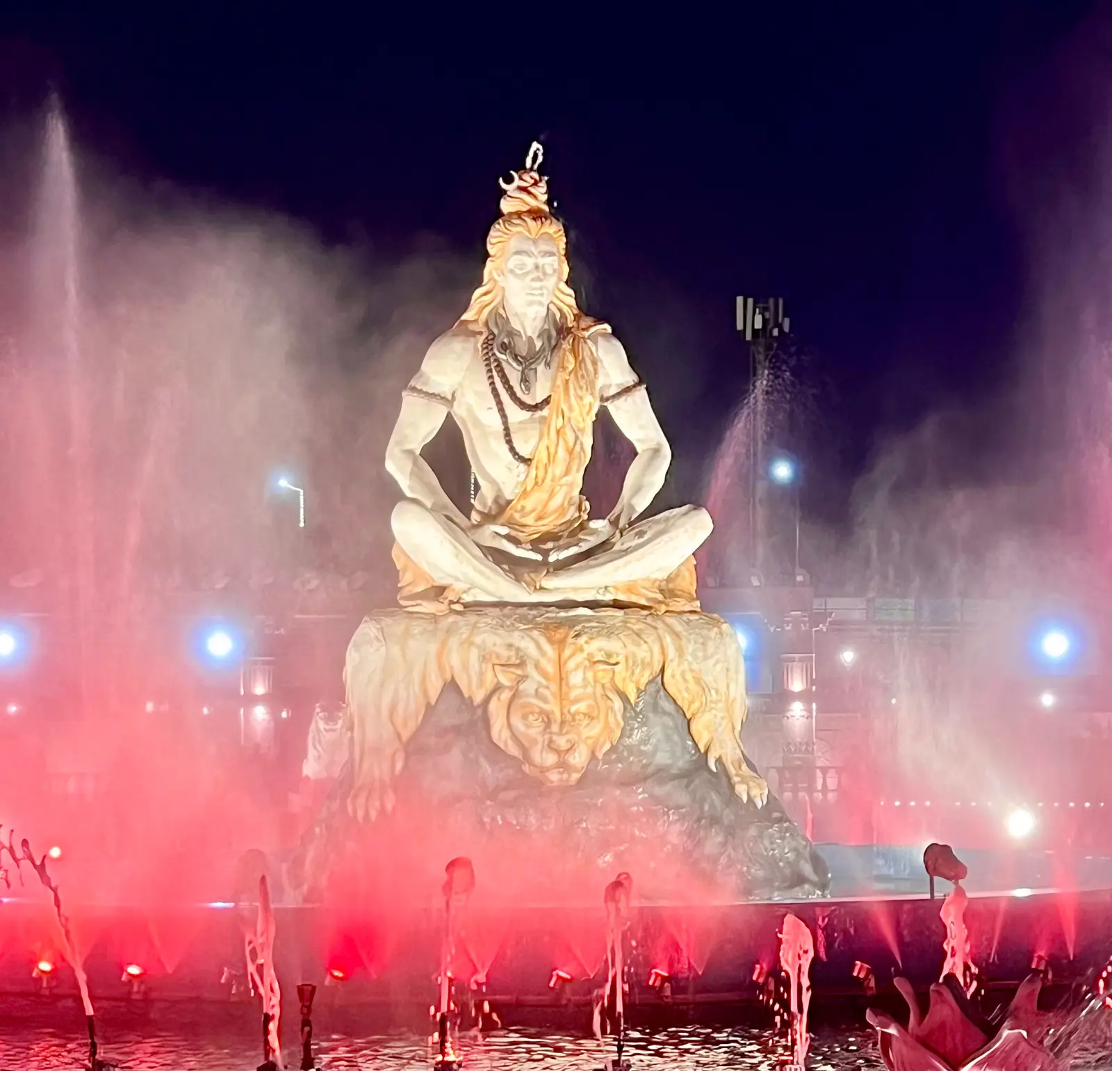 White statue of a seated, meditating Shiva above pink-lit fountains at Mahakal Lok, Ujjain, at night