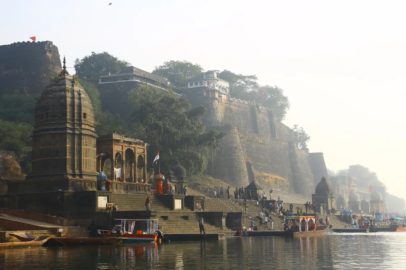 Ahilya Fort walls and a stone riverside temple above the Narmada ghats at Maheshwar, with boats moored below