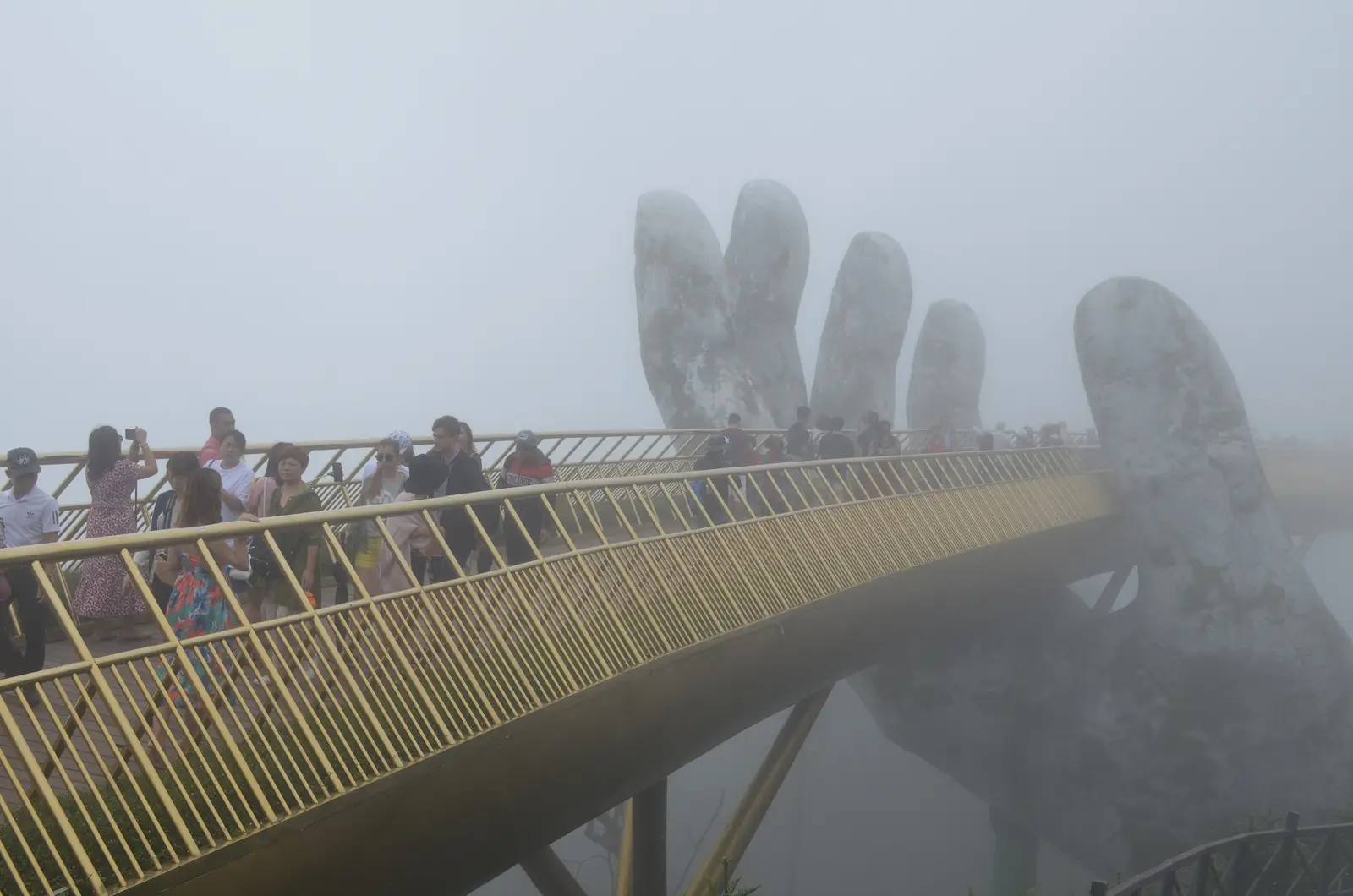 Golden Bridge at Ba Na Hills near Da Nang, held up by two giant stone hands, with visitors crossing in thick mist