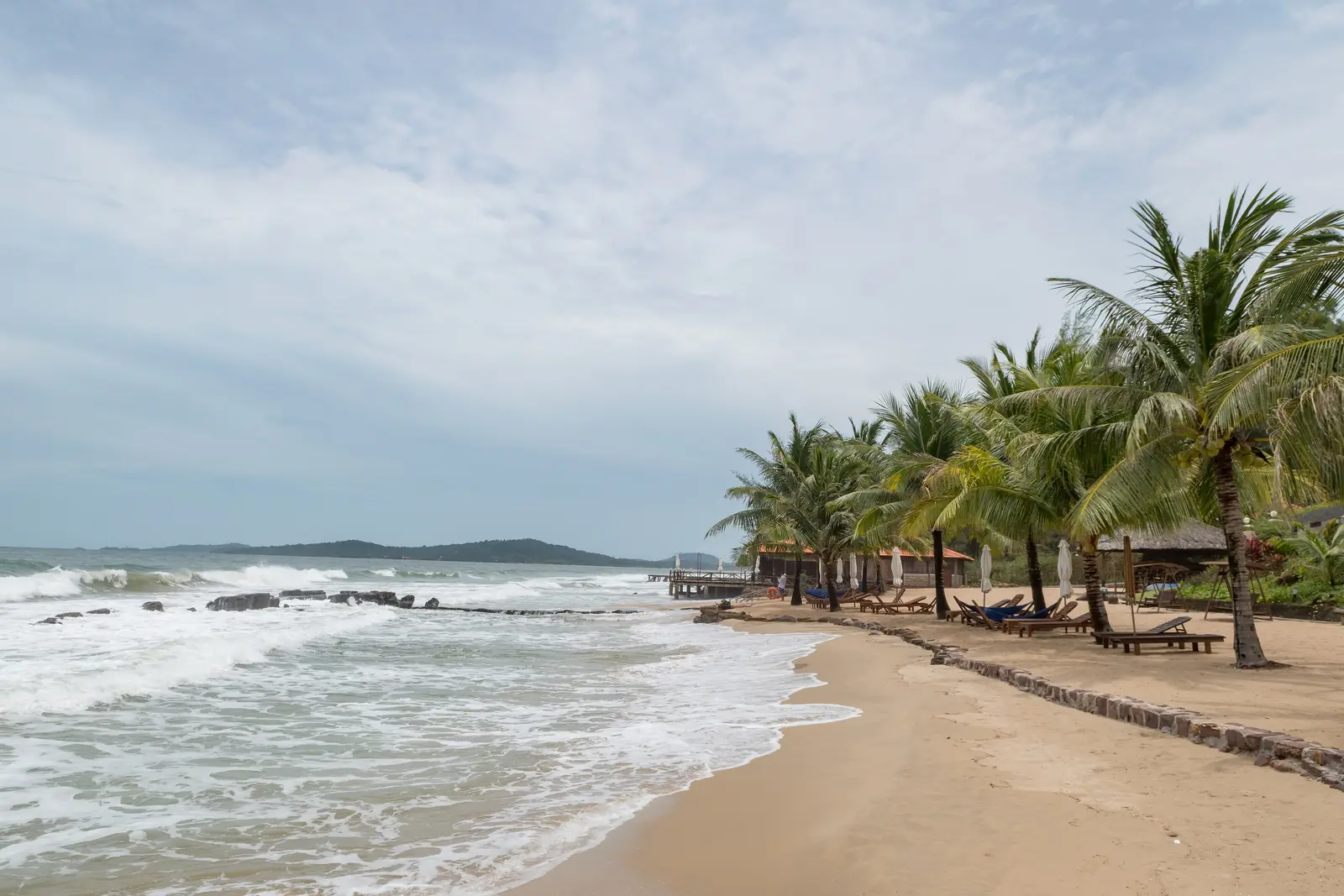 Sandy beach lined with palm trees and sun loungers on Phu Quoc island, Vietnam, under a cloudy sky